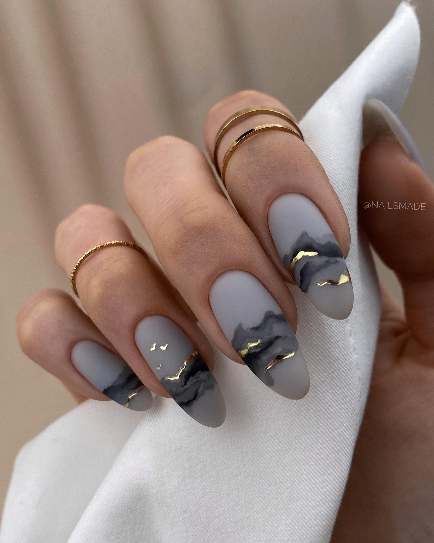 Uñas gris mate con diseño negro y dorado.